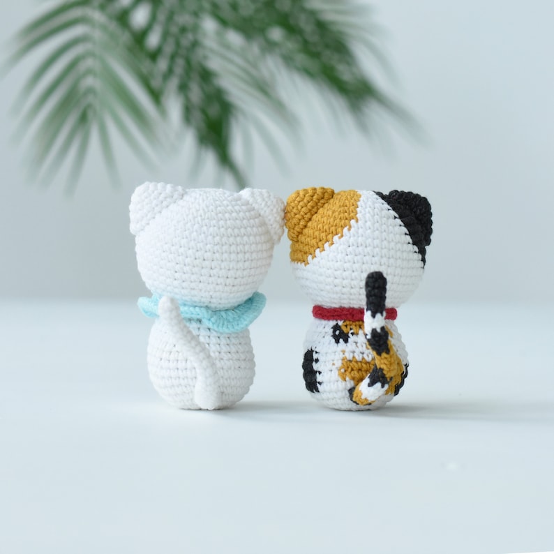 May include: Two crocheted cat toys, one white with a blue collar and one white with orange, black, and brown markings and a red collar.