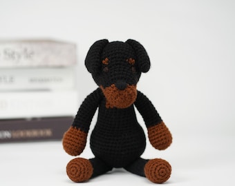 Op de afbeelding: Een gehaakt zwart en bruin Rottweiler knuffeldier dat op een wit oppervlak zit.