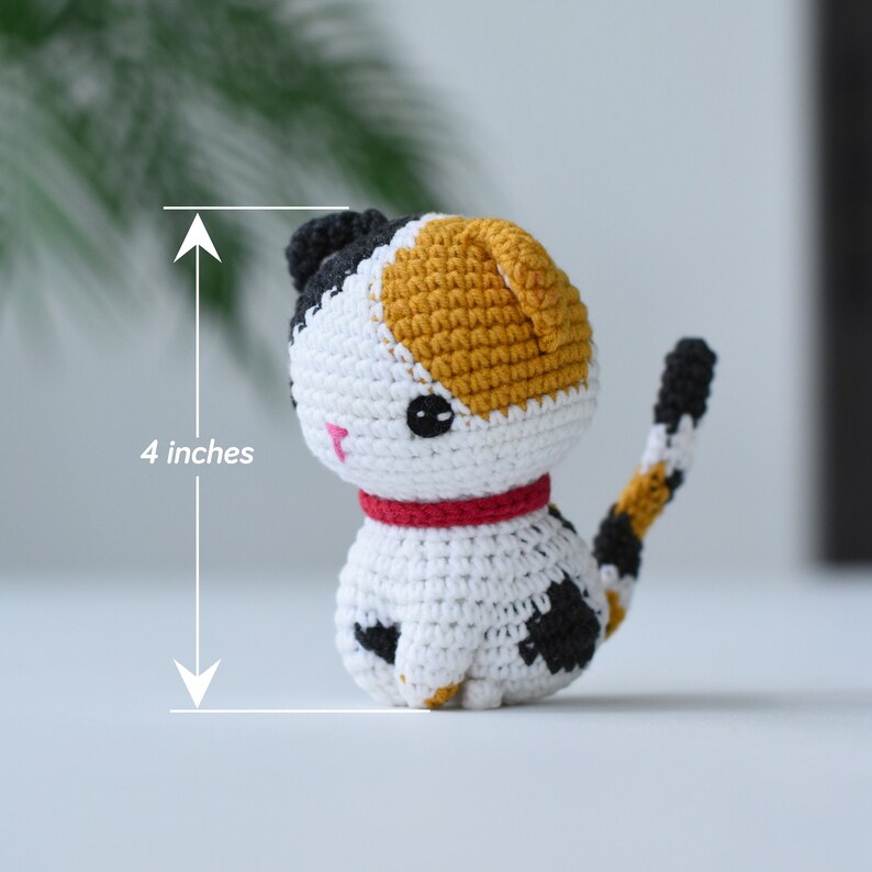 May include: A crocheted calico cat toy, 4 inches tall, with black, white, and orange yarn. The cat has a red collar and black and white spots on its tail.