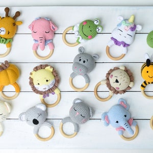 May include: A collection of 15 crocheted animal teethers with wooden rings. The animals include a deer, giraffe, elephant, frog, unicorn, hippopotamus, lion, bee, a pumpkin, a crab, a cat, a koala, an elephant, a monkey and a crocodile.