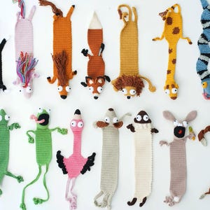 Könnte beinhalten: Eine Sammlung von vierzehn gehäkelten Lesezeichen in Tierform, darunter eine schwarze Katze, ein Fuchs, ein Löwe, eine Giraffe, eine Schlange, eine grüne Eidechse, ein rosa Flamingo und ein braunes Faultier, alle aus Garn in verschiedenen Farben.