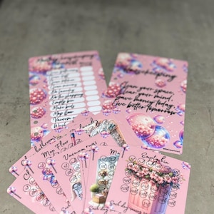 May include: A collection of pink cards with floral and bubble designs. The cards feature handwritten text, including "Clean your space, clear your mind, save money today, live better tomorrow." Some cards have a checklist and others have a calendar.