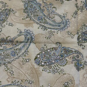 May include: A fabric featuring a repeating paisley pattern in shades of light blue, sage green, and metallic silver on a beige background. The design includes intricate swirling motifs and small floral accents, with a shimmering finish throughout.
