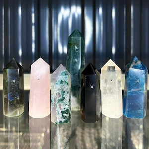 Può includere: Sette punte di cristallo di diversi colori, tra cui verde, blu, nero, rosa e trasparente, sono disposte in fila. Le punte sono alte circa 12,5 cm e hanno una finitura liscia e lucida.