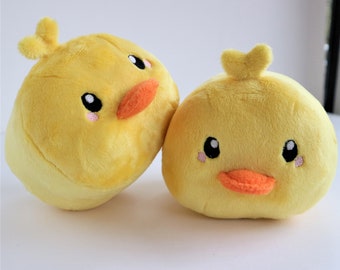 May include: Two plush yellow chick toys with orange beaks, black eyes, and pink cheeks. The chicks have small, heart-shaped tufts on top of their heads. The toys are soft and round, perfect for children.