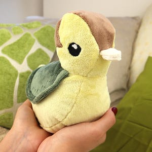 May include: A plush toy in the shape of a turtle. The turtle has a yellow body, a brown head, and a green shell. It has a large black eye and a small white detail on its head. The toy is soft and cuddly.