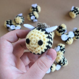 Peut inclure: Une collection de bourdons en crochet de couleur jaune et noire avec des ailes blanches. Les abeilles sont de tailles différentes et sont disposées en cercle sur une surface brune.