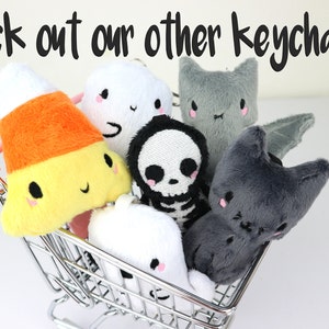 May include: A miniature shopping cart filled with plush Halloween-themed keychains. The keychains include a candy corn, a ghost, a skeleton, a bat, and two cats.