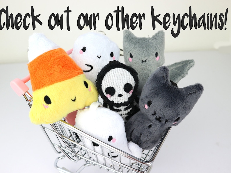 May include: A miniature shopping cart filled with plush Halloween-themed keychains. The keychains include a candy corn, a ghost, a skeleton, a bat, and two cats.