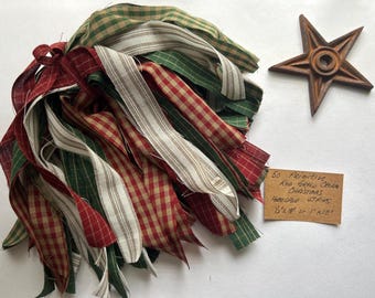 May include: A bundle of red, green, and cream-colored homespun fabric strips, with a star-shaped wooden ornament. The fabric strips are 1/2" x 18" or 1" x 18". A handwritten tag reads "50 Primitive Red Green Cream Christmas Homespun Strips".
