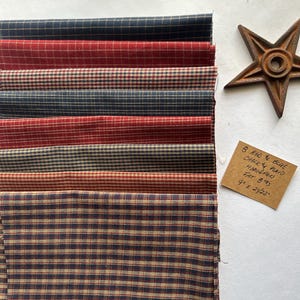 May include: A stack of eight fabric swatches in red, blue, and tan plaid patterns. A rusty metal star is to the right. A small tag reads "8 RED & BLUE CHECK & PLAID HOMESPUN FAT 8THS 9" X 24/22".