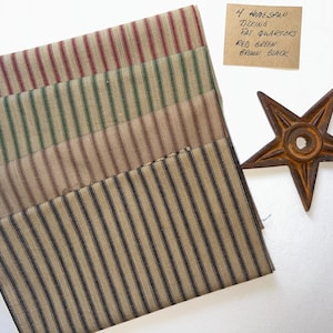 May include: Four homespun ticking fat quarters with red, green, brown, and black stripes. A rusty metal star is next to the fabric. The fabric is folded and stacked. A handwritten note indicates the fabric colours.