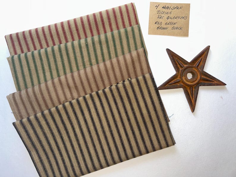 May include: Four homespun ticking fat quarters with red, green, brown, and black stripes. A rusty metal star is next to the fabric. The fabric is folded and stacked. A handwritten note indicates the fabric colours.