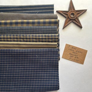 May include: A collection of seven blue and tan fabric swatches with various patterns, including stripes and checks. A rusty metal star and a handwritten tag that reads "7 Blue Check Stripe Flannel Homespun Fat Bits 9" x 21/22"" are also present.