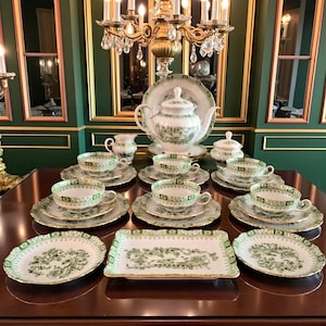 Puede incluir: Un juego de té antiguo completo con un patrón floral verde. El juego incluye una tetera, azucarero, crema, tazas, platillos y fuentes. Los bordes de los platos y tazas tienen un borde dorado.