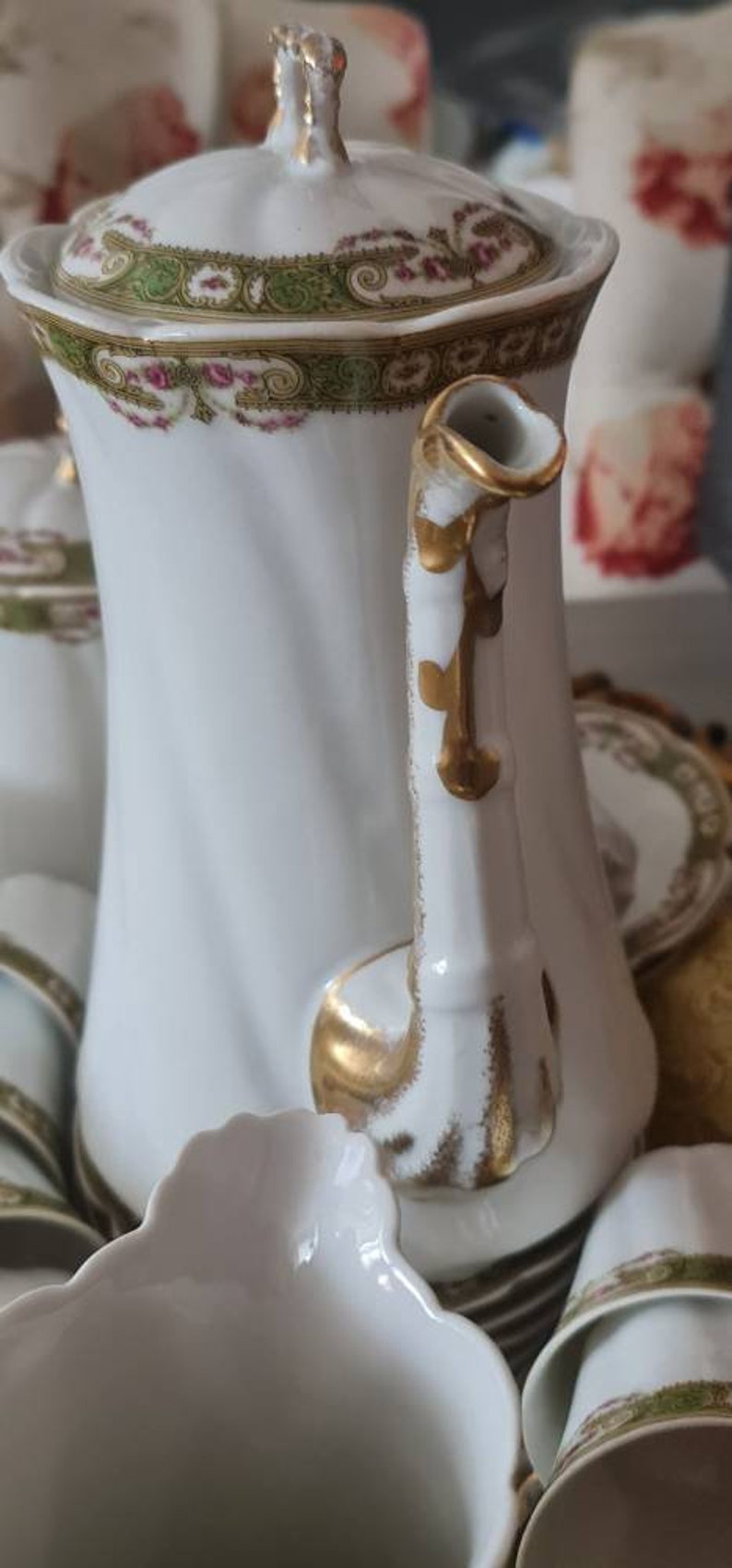 May include: White porcelain tea set with gold accents and floral detailing. The set includes a teapot with a lid, cups, and saucers. The teapot handle and lid finial are gold. The set has a vintage aesthetic.