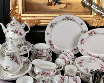 Puede incluir: Un juego de vajilla de porcelana blanca con un patrón floral en tonos rosa y verde. El juego incluye una tetera, una jarra de crema, un azucarero, platos, cuencos y una fuente para servir.