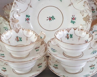 May include: A set of vintage porcelain teacups and saucers with delicate floral designs in red, green, and gold. The set includes a large serving platter with a similar floral pattern.