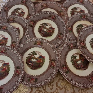 May include: A set of 10 brown and white ceramic dinner plates with a floral pattern and a scene of a castle and trees.
