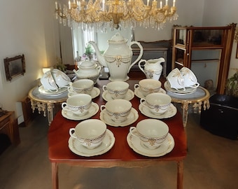 May include: A white porcelain tea set with gold trim and black accents. The set includes a teapot, creamer, sugar bowl, and six teacups and saucers.