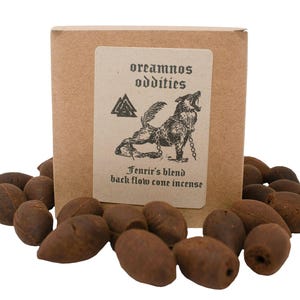 Puede incluir: Una caja de papel kraft con una etiqueta que presenta una ilustración de un lobo aullando y el texto "oreamnos oddities Fenrir's blend back flow cone incense". La caja está rodeada de numerosos conos de incienso marrones.
