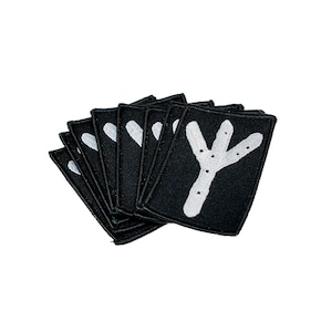 May include: A stack of black fabric patches with white embroidered symbols. Each patch is rectangular with rounded corners. The symbols are stylized, resembling runes or ancient markings. The patches are arranged in a fan shape, showcasing the designs.