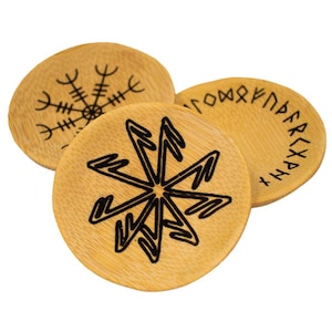 May include: Three wooden coasters with black etched designs. One coaster features a snowflake-like symbol, another has a starburst pattern, and the third displays runes. The coasters are circular and made of light-colored wood.