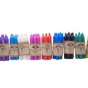 May include: Bundles of colorful taper candles in orange, purple, blue, white, pink, red, blue, black, green, and yellow. Each bundle is wrapped with twine and a brown paper label. A black candle holder is also present.