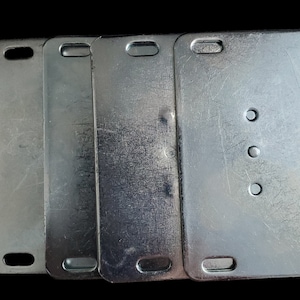 May include: Four rectangular, silver metal plates with rounded corners and a hole at the top. The plates have varying surface textures and some have three circular holes. The plates are arranged side by side.