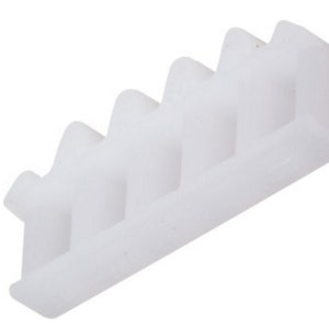 May include: White plastic molding with a series of five teeth or ridges on the top. The molding is rectangular in shape and has a smooth, slightly rounded surface.