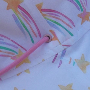 May include: White fabric with a pink drawstring and a repeating pattern of yellow stars with rainbow trails.