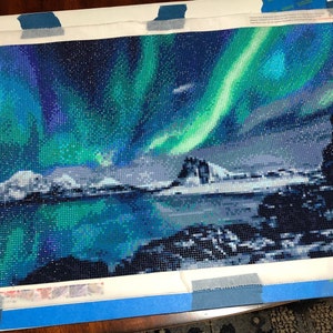 Peut inclure: Une peinture de diamant terminée représentant un paysage pittoresque avec une aurore boréale vibrante dans le ciel au-dessus d'une chaîne de montagnes enneigées et d'un plan d'eau réfléchissant.