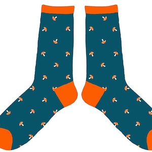 Puede incluir: Un par de calcetines de media caña en color verde azulado oscuro con un patrón repetitivo de pequeños hongos naranjas con puntos blancos. Los calcetines tienen puños, talones y punteras de color naranja sólido que contrastan con el tejido.