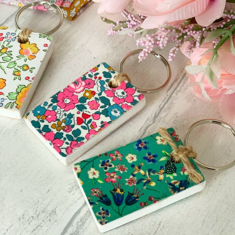 May include: Three floral patterned keychains with silver key rings. The keychains are rectangular and have a white background with colorful floral patterns.