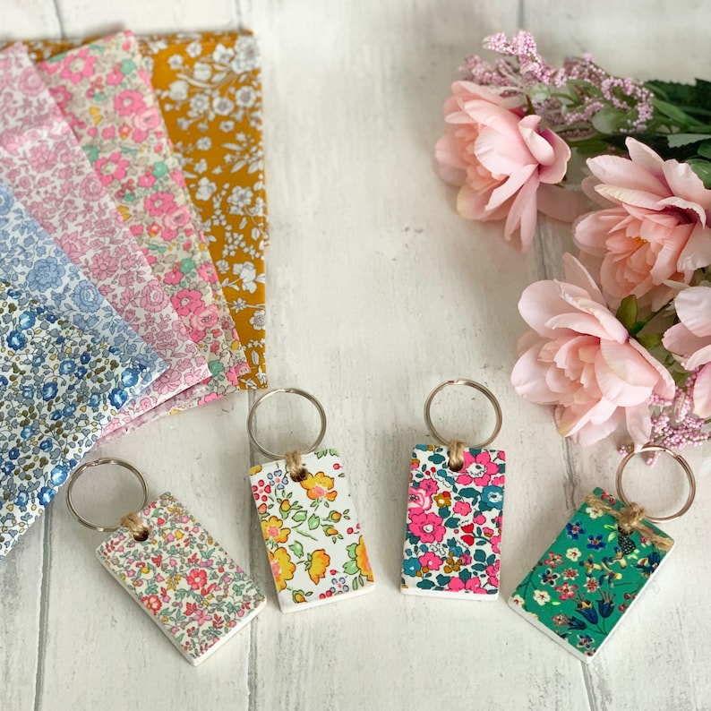 May include: Four floral patterned keychains with silver key rings. The keychains are rectangular and feature different floral patterns in shades of pink, blue, green, and yellow.