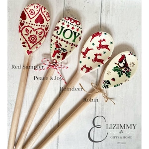 Puede incluir: Cuatro cucharas de madera con cuencos de color crema con motivos festivos. La primera tiene corazones rojos, la segunda dice JOY, la tercera tiene renos rojos y la cuarta muestra un petirrojo con hojas de acebo verdes.