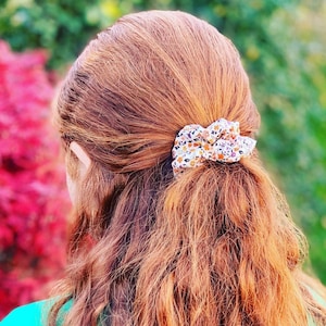 A red haired young lady models one of our scrunchies in an autumnal design which has small orange, yellow and purple flowers on it. The photo is taken from behind the model and shows how the scrunchie looks with half the hair up and half down.