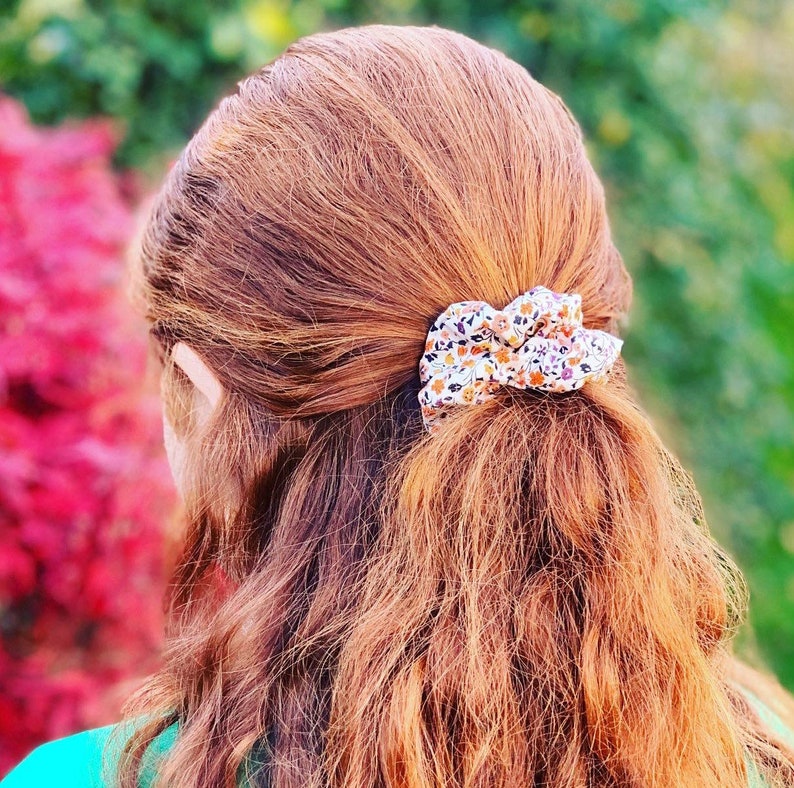 A red haired young lady models one of our scrunchies in an autumnal design which has small orange, yellow and purple flowers on it. The photo is taken from behind the model and shows how the scrunchie looks with half the hair up and half down.