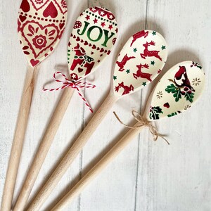 Puede incluir: Cuatro cucharas de madera con patrones decorativos en los cuencos. Una tiene corazones rojos, otra dice JOY con un caballo, otra tiene renos rojos y una muestra un p&aacute;jaro sobre acebo. Dos cucharas est&aacute;n atadas con cuerda o cordel.