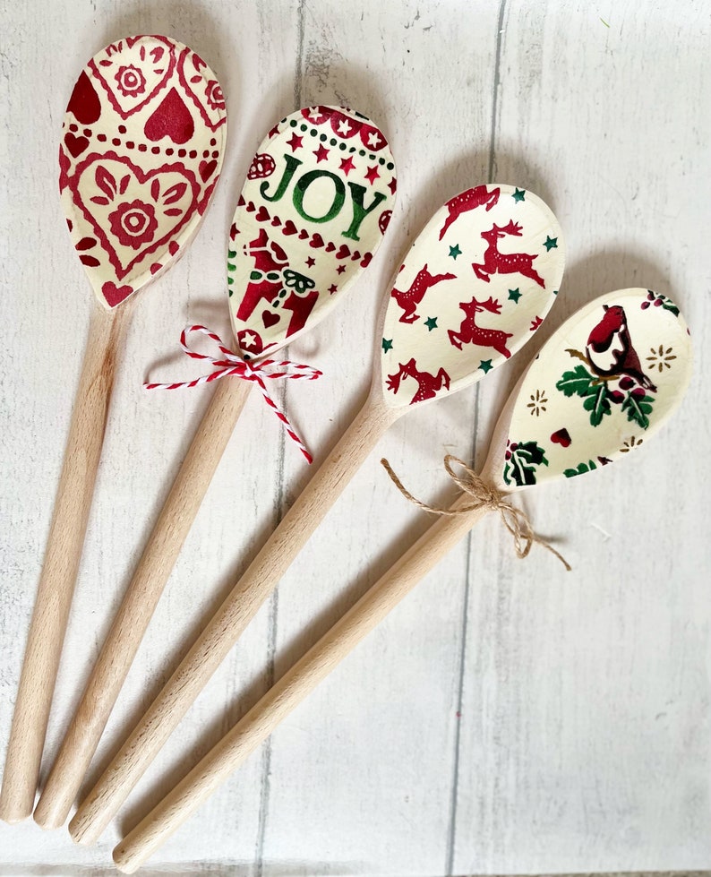 Puede incluir: Cuatro cucharas de madera con patrones decorativos en los cuencos. Una tiene corazones rojos, otra dice JOY con un caballo, otra tiene renos rojos y una muestra un p&aacute;jaro sobre acebo. Dos cucharas est&aacute;n atadas con cuerda o cordel.