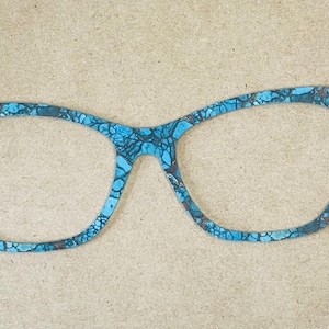 May include: A flat, two-dimensional cutout in the shape of cat-eye glasses. The surface features a vibrant turquoise and blue mosaic pattern with dark, intricate veining that resembles cracked stone or a detailed geological texture throughout.