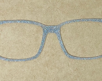 May include: A pair of eyeglasses with a glittery, light blue finish. The glasses have a classic rectangular frame shape. The image is set against a neutral, light brown background.