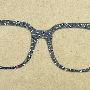 May include: A pair of eyeglasses with a black and white pirate-themed pattern. The design includes skulls, ship wheels, and red accents. The glasses are set against a neutral background.