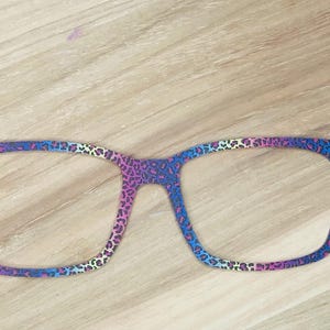 May include: A pair of colorful glasses with a leopard print design. The glasses are made of plastic and have a rainbow gradient.