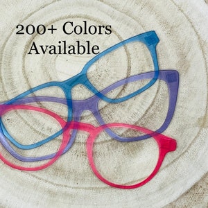 May include: Three pairs of clear plastic eyeglasses in different colors: blue, purple, and pink. The text "200+ Colors Available" is visible in the image.