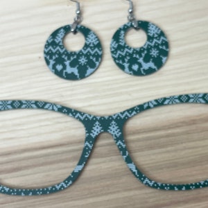 Puede incluir: Un par de gafas de pasta verde y blanca con un patrón y un par de pendientes a juego verde y blanco. Los pendientes son de forma ovalada con un gancho plateado.