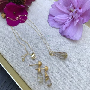 K&ouml;nnte beinhalten: Ein Schmuckset aus Gold mit tropfenf&ouml;rmigen, klaren Quarzsteinen. Das Set enth&auml;lt eine Halskette und ein Paar Ohrringe.
