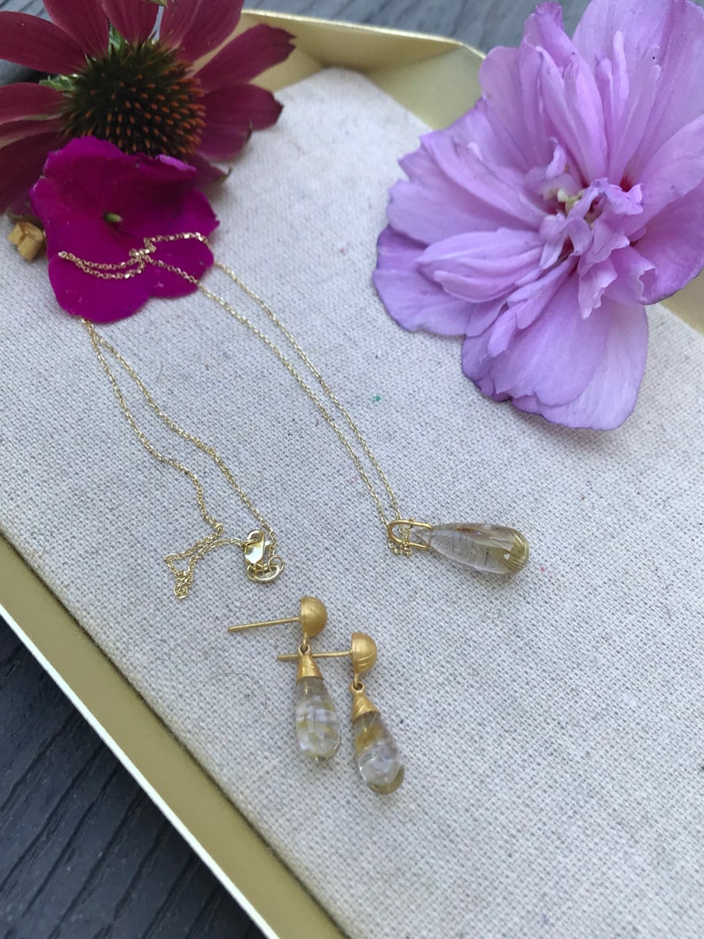 K&ouml;nnte beinhalten: Ein Schmuckset aus Gold mit tropfenf&ouml;rmigen, klaren Quarzsteinen. Das Set enth&auml;lt eine Halskette und ein Paar Ohrringe.