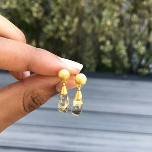 K&ouml;nnte beinhalten: Goldene und klare Tropfenohrringe mit einer goldenen Kugel oben.