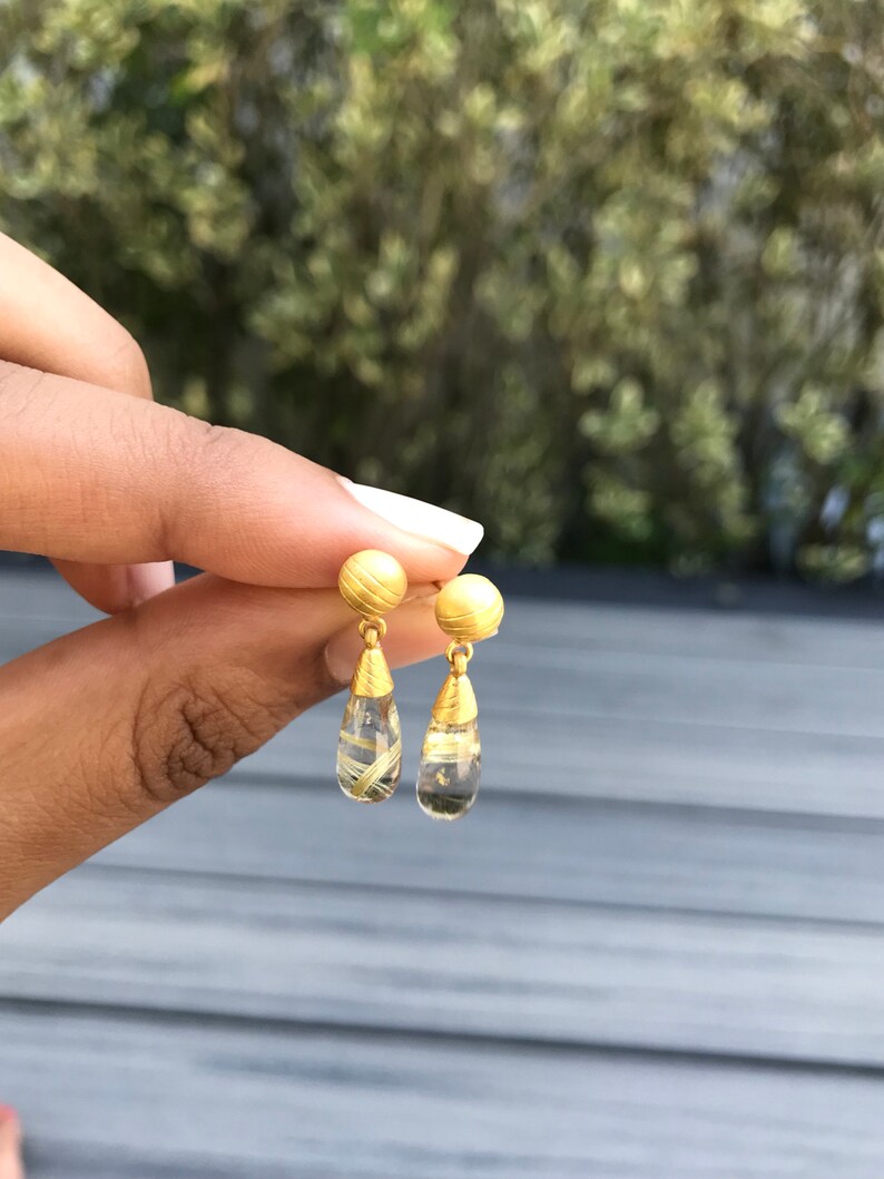 K&ouml;nnte beinhalten: Goldene und klare Tropfenohrringe mit einer goldenen Kugel oben.